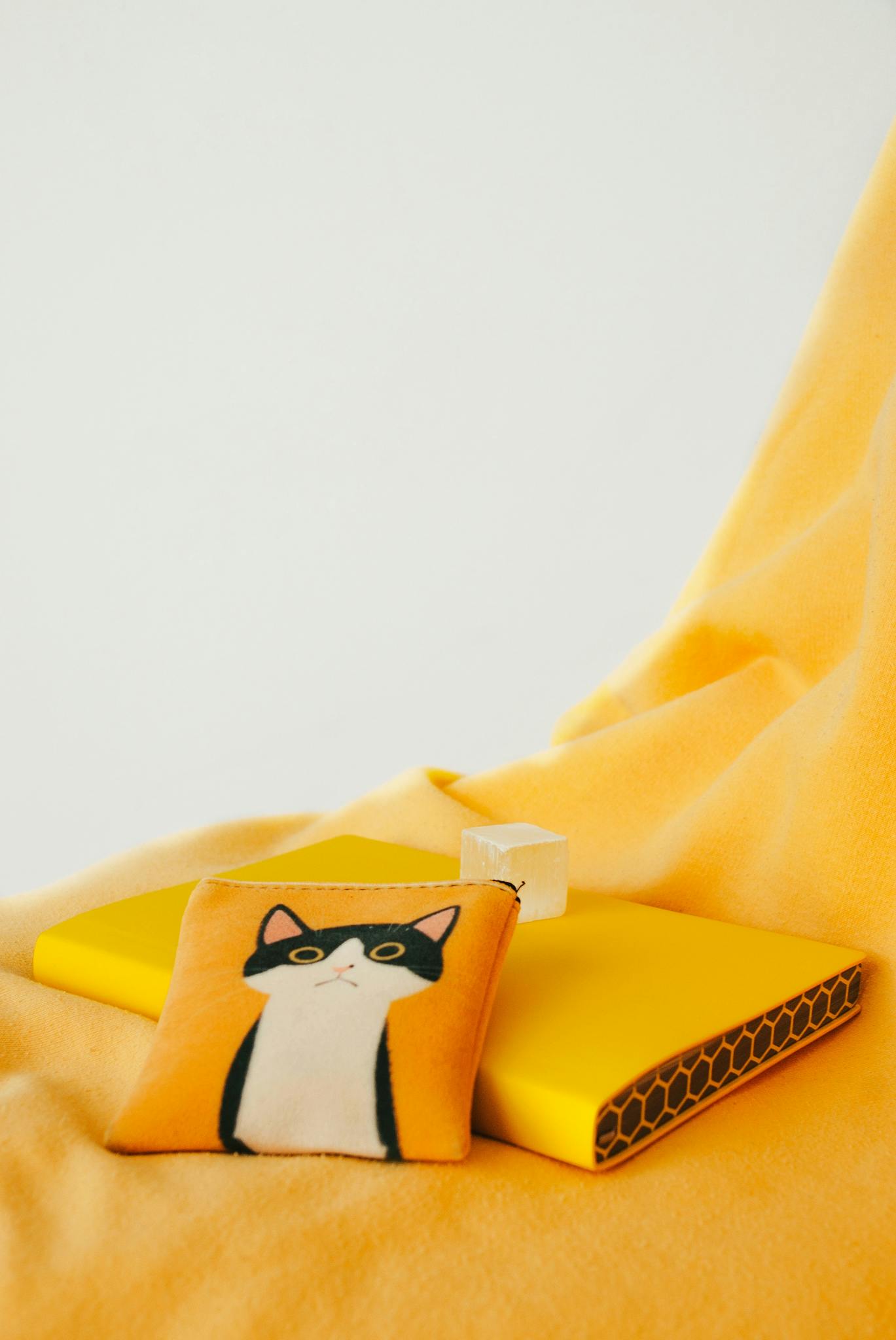 A cute cat coin purse rests on bright yellow fabric, creating a playful still life scene.
